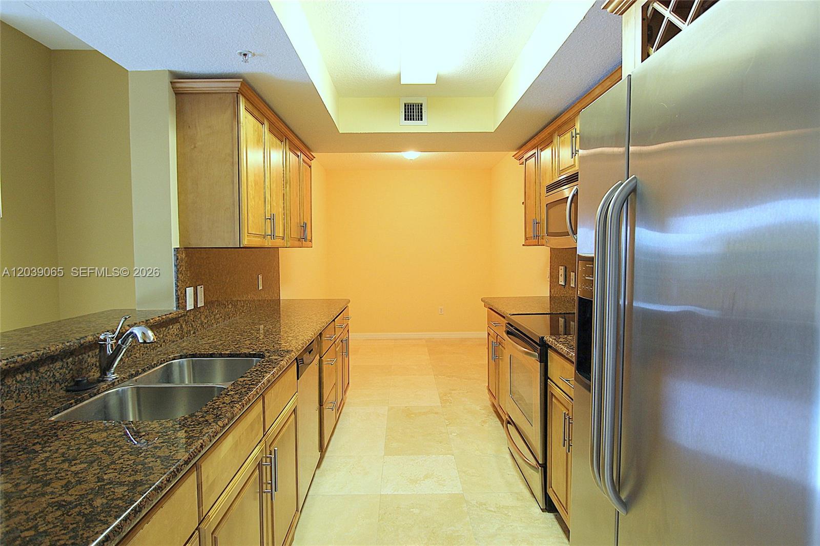 A galley kitchen features light wood cabinets, granite countertops, and stainless steel appliances — 3530 SW 22nd St # 505, Miami FL 33145, MIAMI, FL