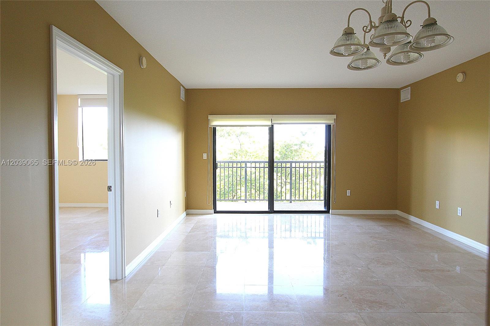 An empty living room features tan walls, polished tile flooring, a chandelier, and sliding glass doors — 3530 SW 22nd St # 505, Miami FL 33145, MIAMI, FL