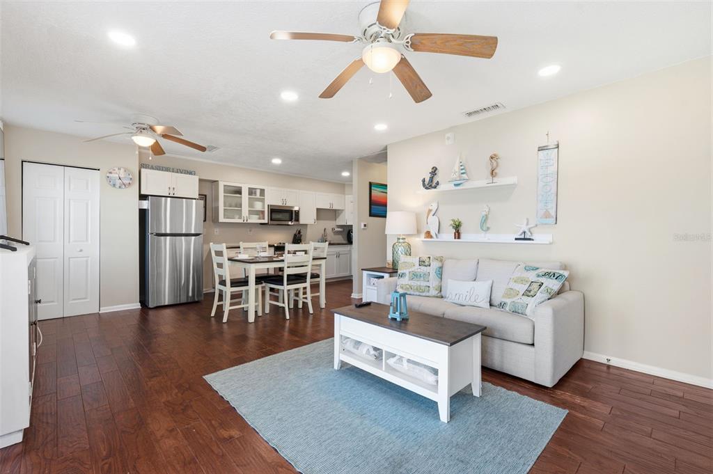 An open-concept living and dining area features wood-look flooring, a ceiling fan, and coastal decor — 5117 SALMON DRIVE SE UNIT B, ST PETERSBURG, FL