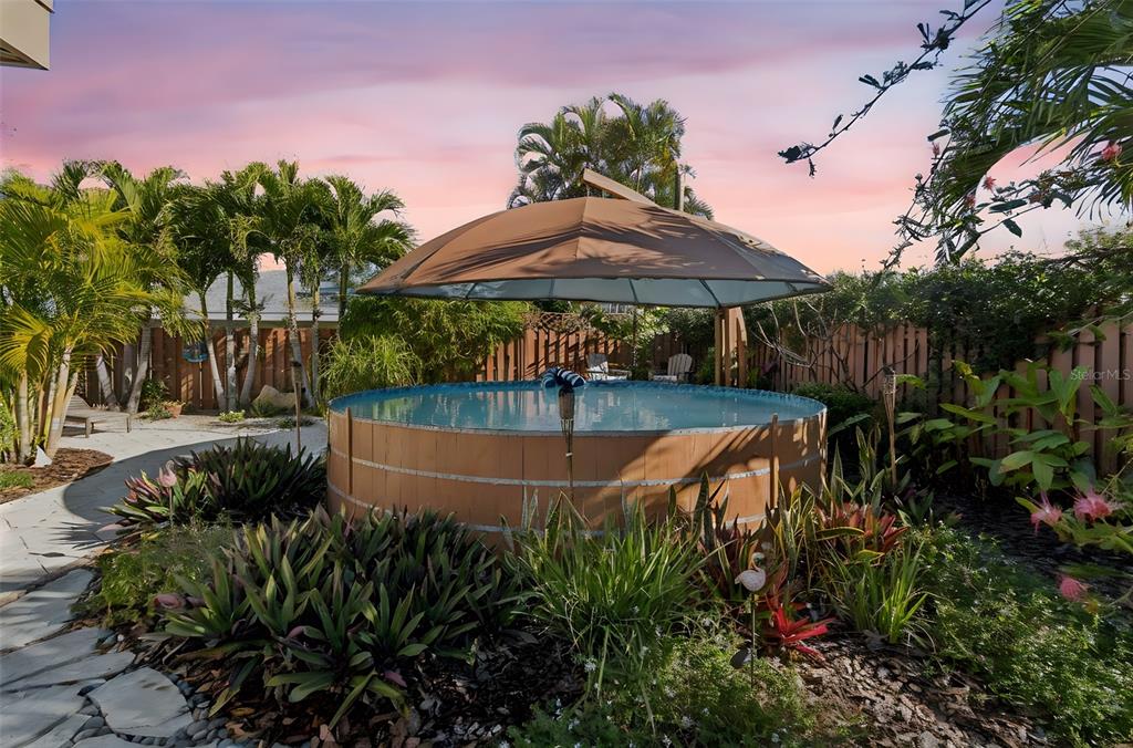 A round above-ground pool with a brown umbrella sits in a landscaped backyard at sunset — 618 WHITFIELD AVENUE, SARASOTA, FL