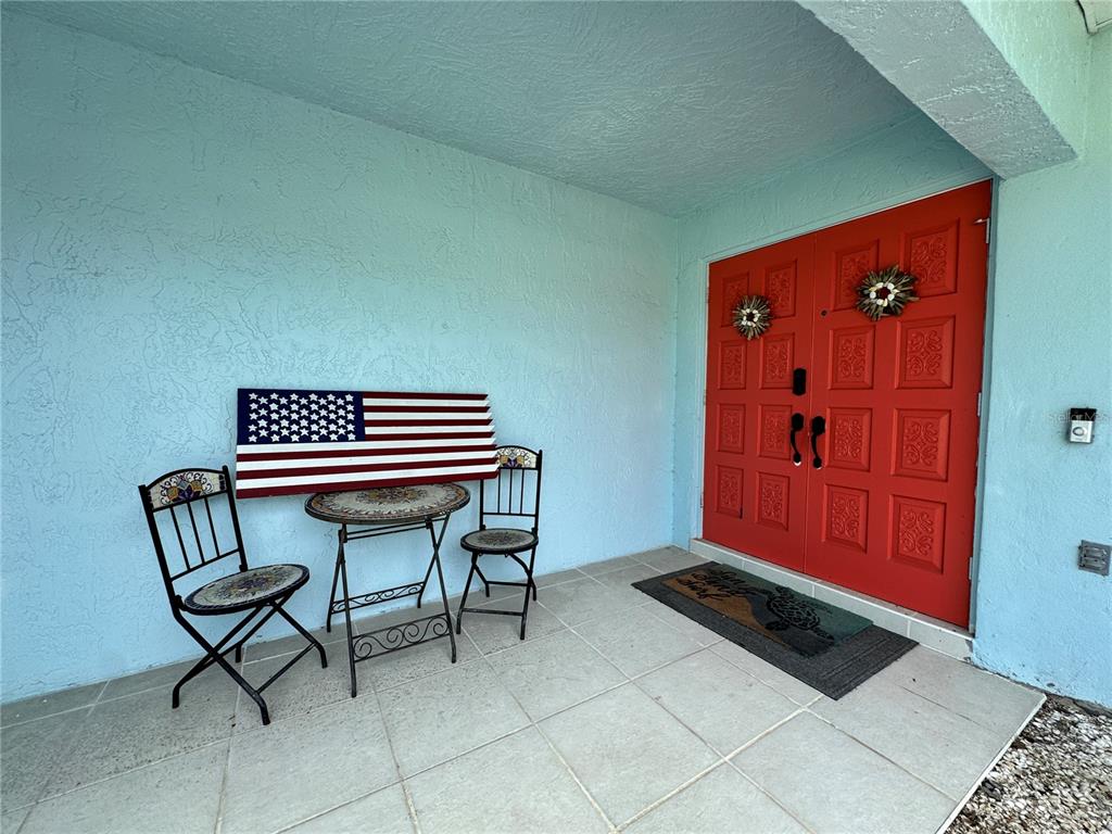 A front porch features a small bistro set, a wall-mounted American flag, and red double doors — 6813 13TH AVENUE DRIVE W, BRADENTON, FL