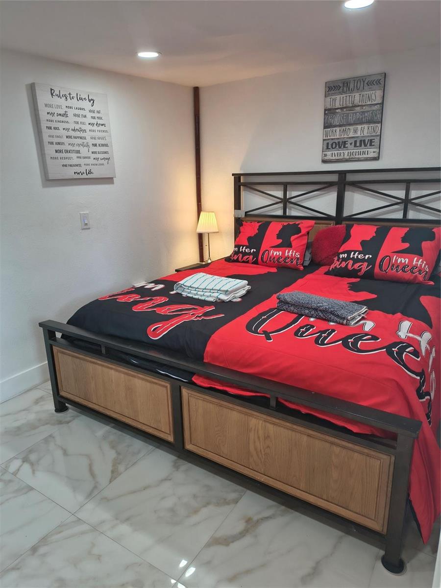 A bedroom features a metal-framed bed with red and black bedding and marble-look flooring — 2206 Coolidge Street Unit B, Hollywood FL 33020, HOLLYWOOD, FL
