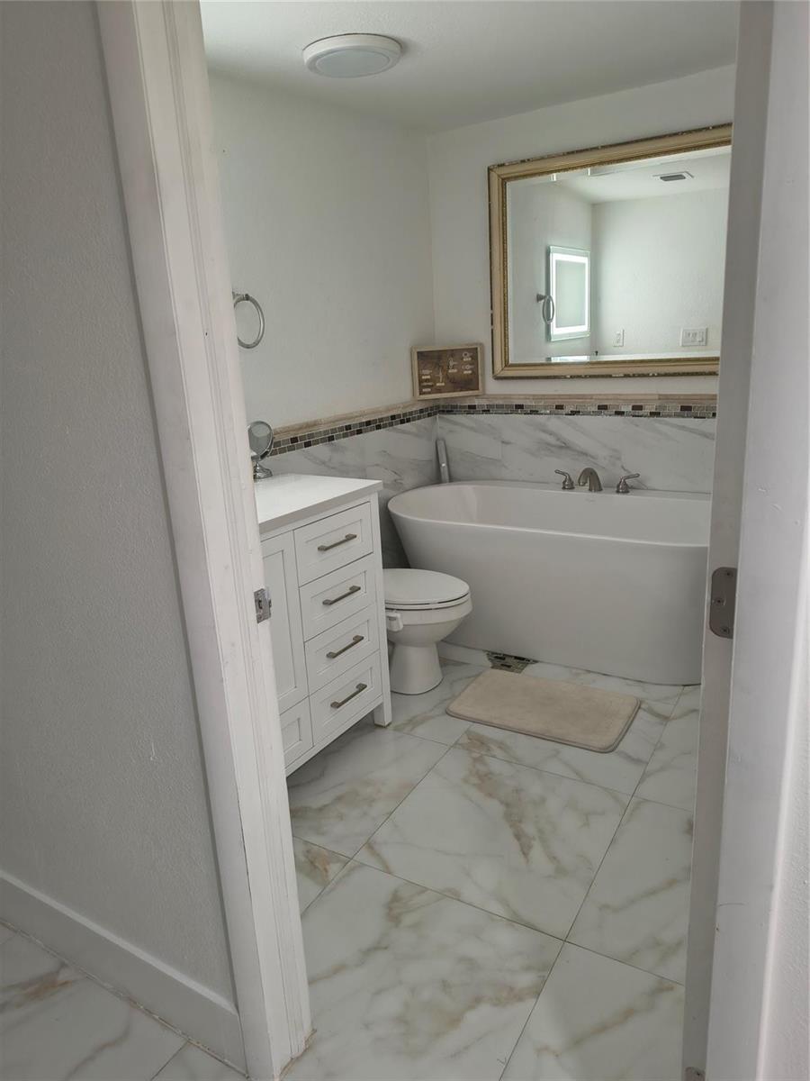 A bathroom features a white vanity, a freestanding tub, and marble-look tile flooring and walls — 2206 Coolidge Street Unit B, Hollywood FL 33020, HOLLYWOOD, FL