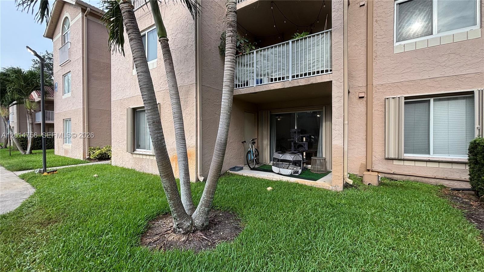 The exterior of a multi-story apartment building features a ground-level patio with a bicycle — 10420 SW 158th Ct # 105, Miami FL 33196, MIAMI, FL