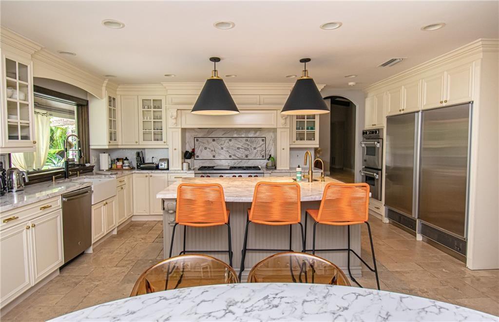 A kitchen features cream cabinets, a marble-topped island with orange stools, and stainless steel appliances — 8208 Twin Lake Drive, Boca Raton FL 33496, BOCA RATON, FL