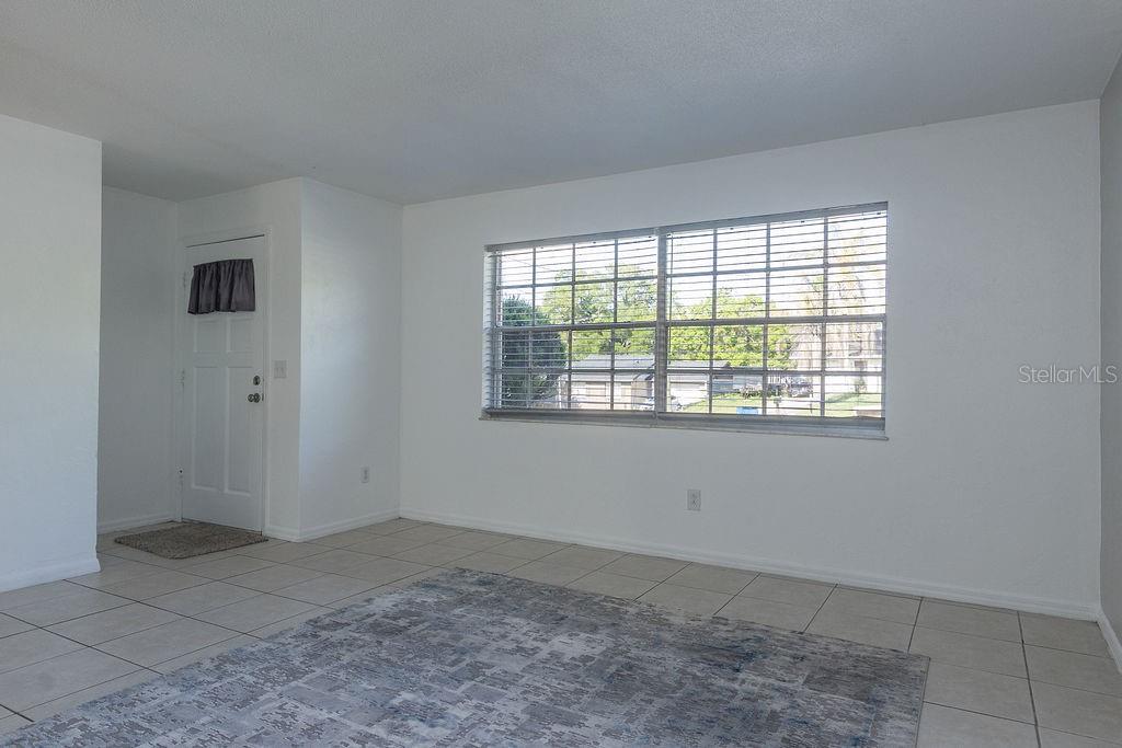A living room with white walls, tiled floors, a large window, and a front door — 1516 S BOUNDARY STREET, DELAND, FL
