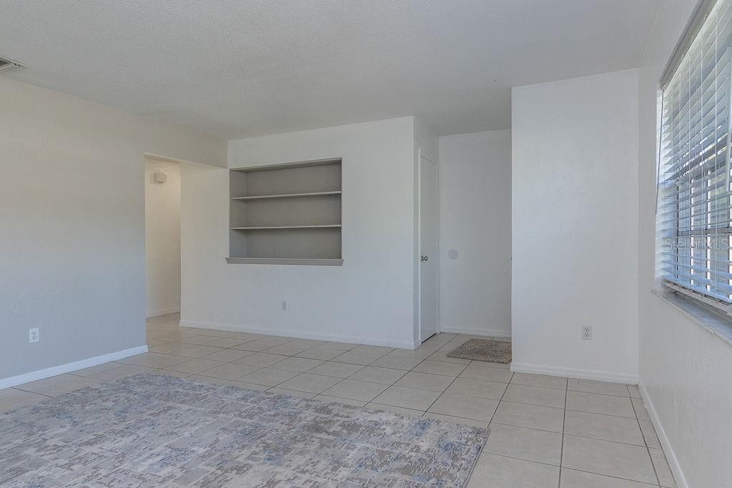 A living room with light-colored tile flooring, white walls, built-in shelving, and a large window — 1516 S BOUNDARY STREET, DELAND, FL
