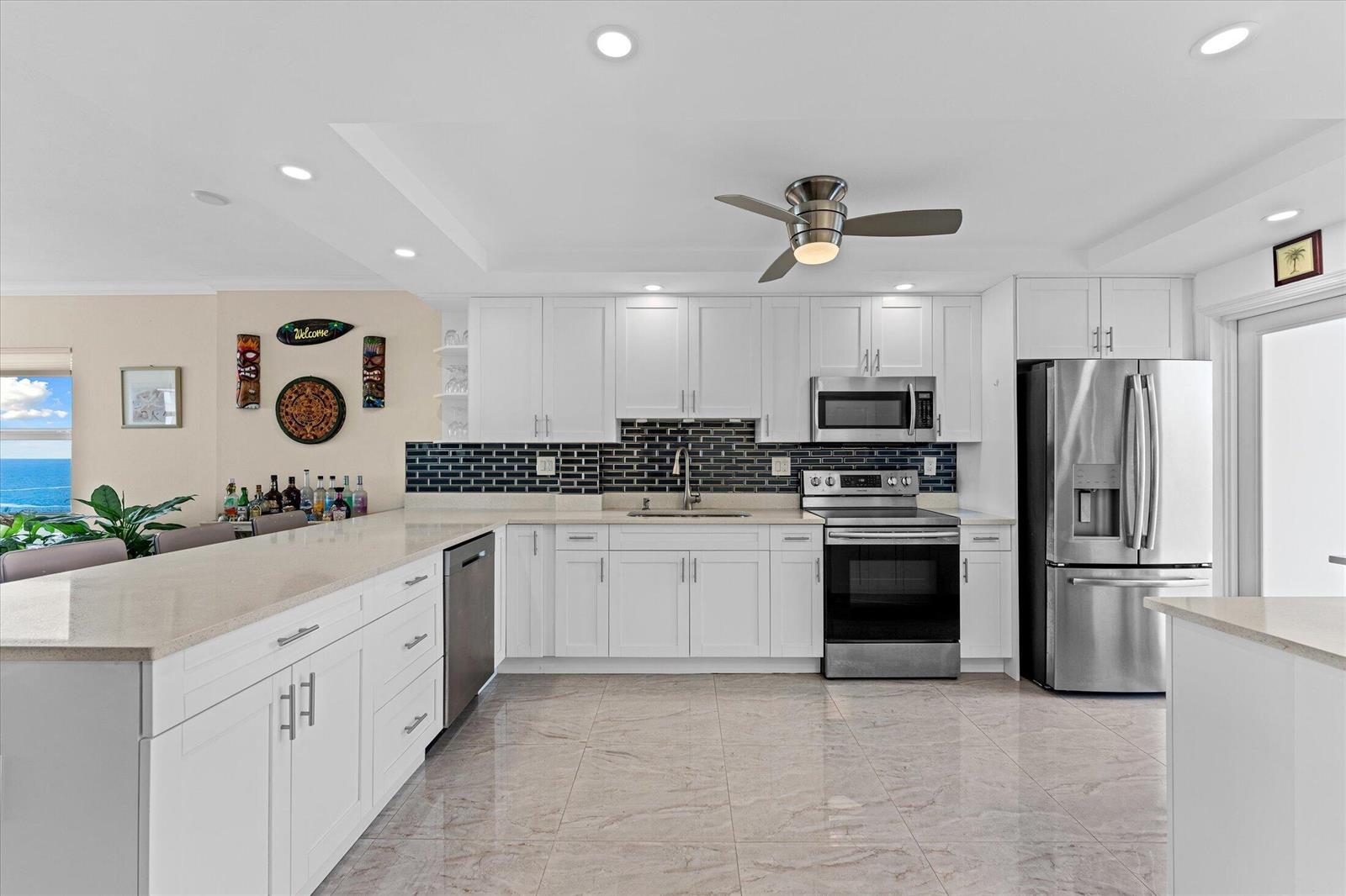 A modern kitchen features white cabinets, stainless steel appliances, a dark tile backsplash, and tile flooring — 750 N Ocean Boulevard # 710, Pompano Beach FL 33062, POMPANO BEACH, FL