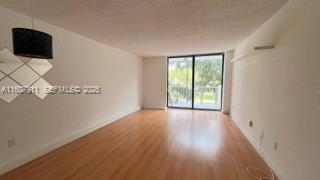 An empty living room with light wood-look flooring, white walls, and a sliding glass door — 2350 NE 135th St # 212, North Miami FL 33181, NORTH MIAMI, FL