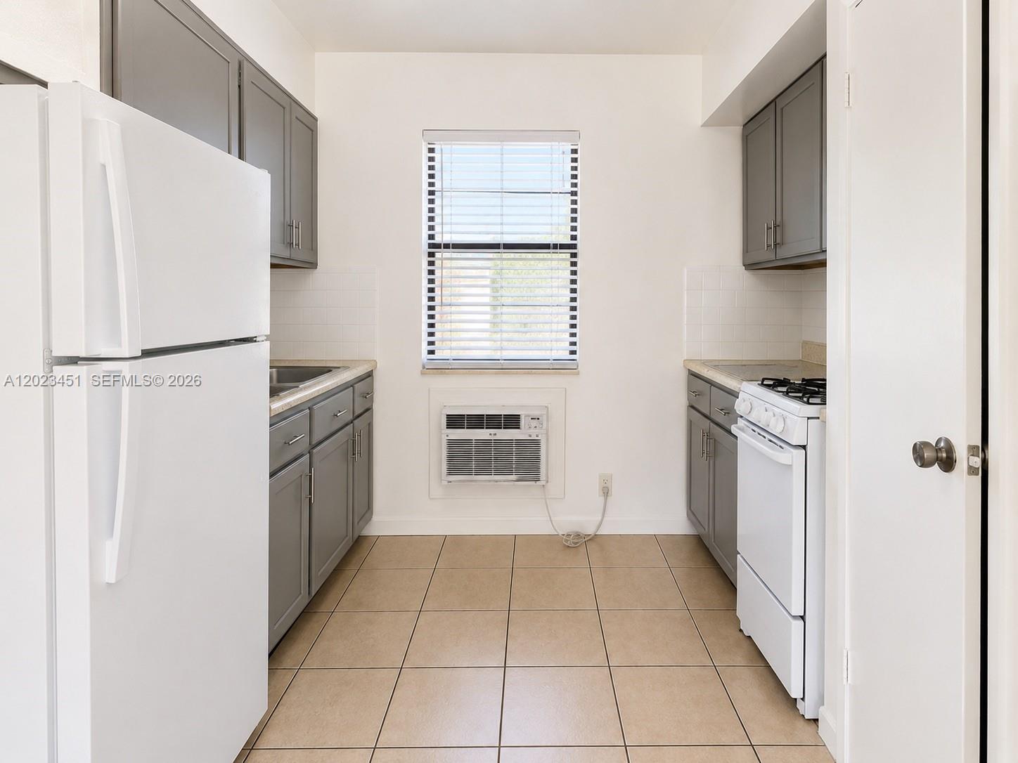 A galley-style kitchen features gray cabinets, white appliances, tiled flooring, and a window air conditioner — 1741-1743 Moffett St, Hollywood FL 33020, HOLLYWOOD, FL