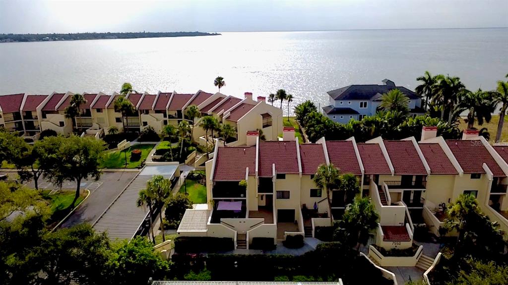 An aerial view shows multi-story townhomes with red roofs situated along a waterfront — 7550 SUNSHINE SKYWAY LANE S UNIT P11, ST PETERSBURG, FL