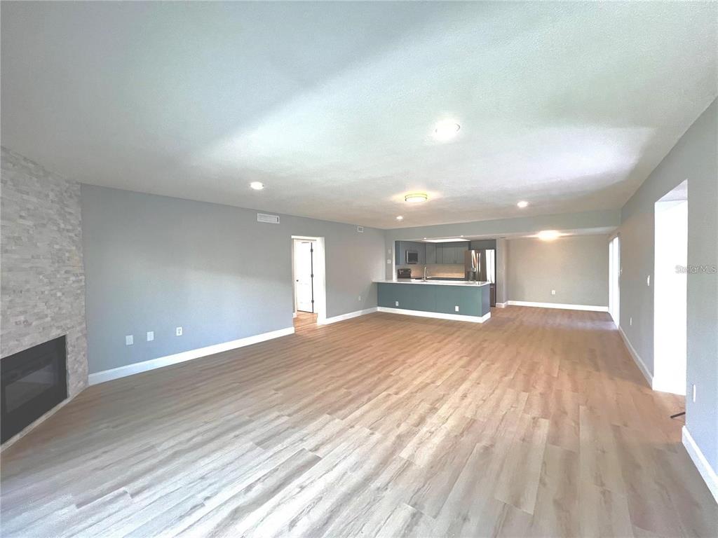 A spacious living room features light wood-look flooring, a stone fireplace, and an open kitchen — 7550 SUNSHINE SKYWAY LANE S UNIT P11, ST PETERSBURG, FL