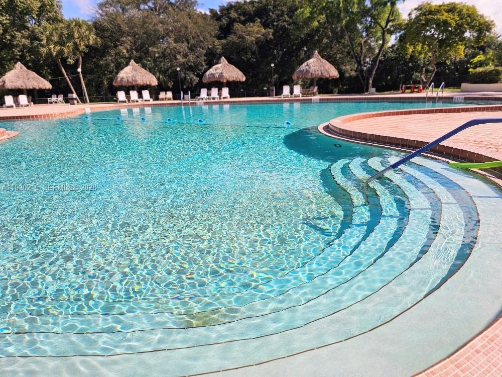 An outdoor swimming pool with tiered steps and several thatched-roof umbrellas on the deck — 3100 Holiday Springs Blvd # 304, Margate FL 33063, MARGATE, FL