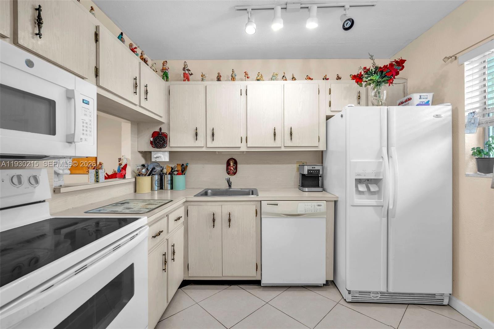 A kitchen features white appliances, light wood cabinets, tile flooring, and a track lighting fixture — 3100 Holiday Springs Blvd # 304, Margate FL 33063, MARGATE, FL