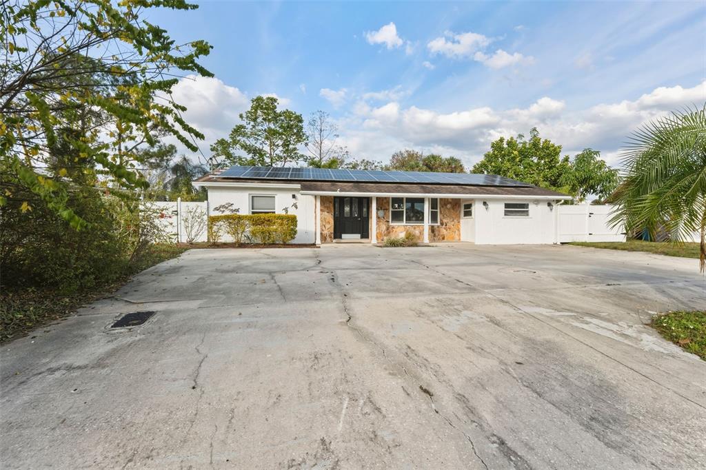 A single-story house with a large concrete driveway, stone facade, and roof-mounted solar panels — 5017 STOLLS AVENUE, TAMPA, FL
