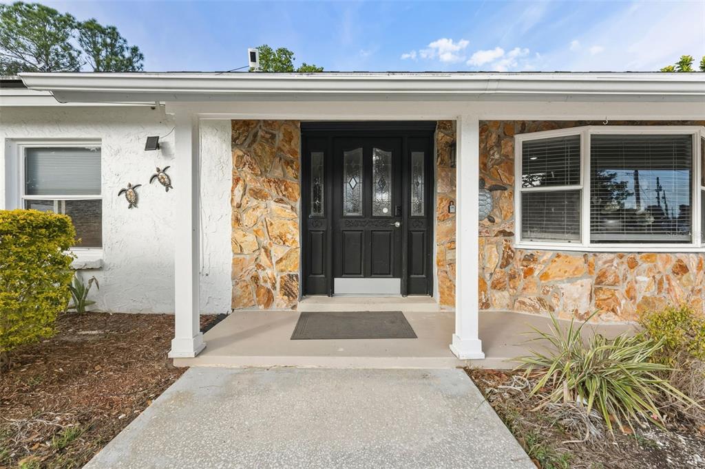 The exterior of a house features a covered porch, a black door, and stone siding — 5017 STOLLS AVENUE, TAMPA, FL