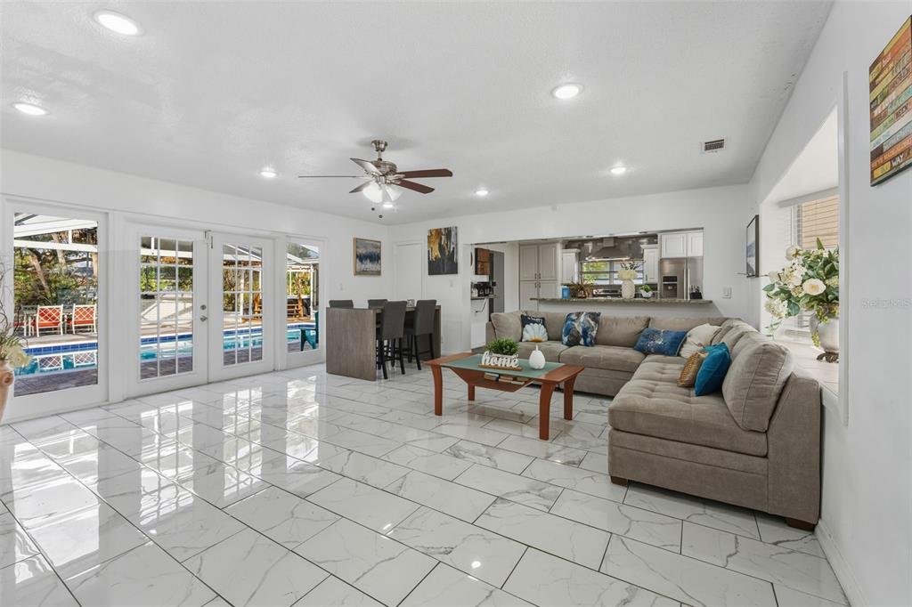 An open-concept living and dining area features white marble-look tile floors and a backyard pool — 5017 STOLLS AVENUE, TAMPA, FL