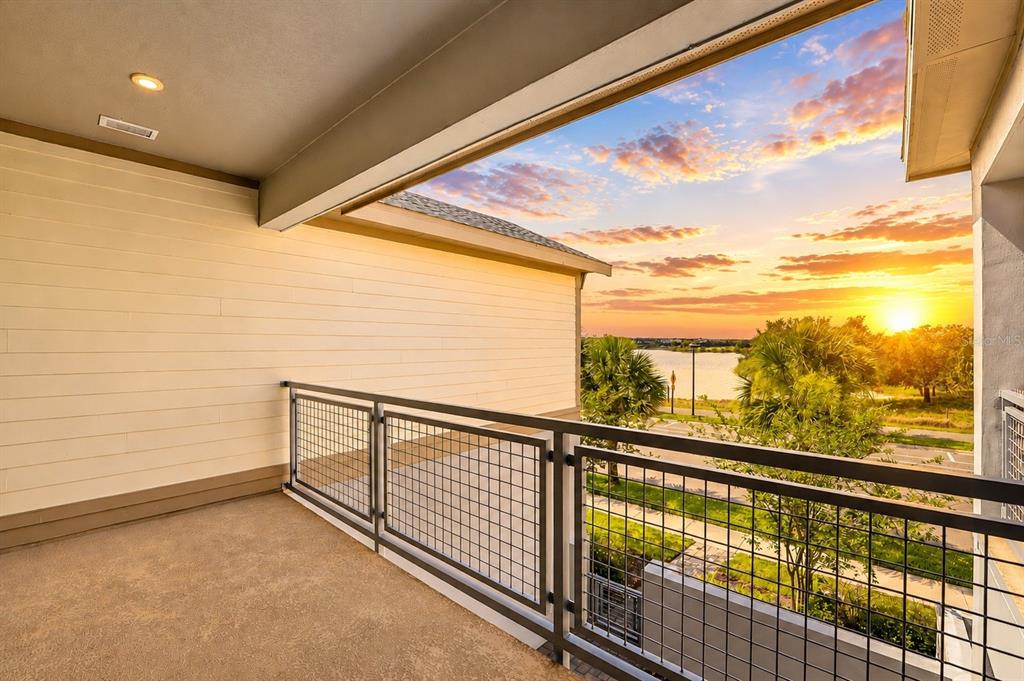 A covered balcony with a metal railing overlooks a lake at sunset — 7227 NEMOURS PARKWAY, ORLANDO, FL