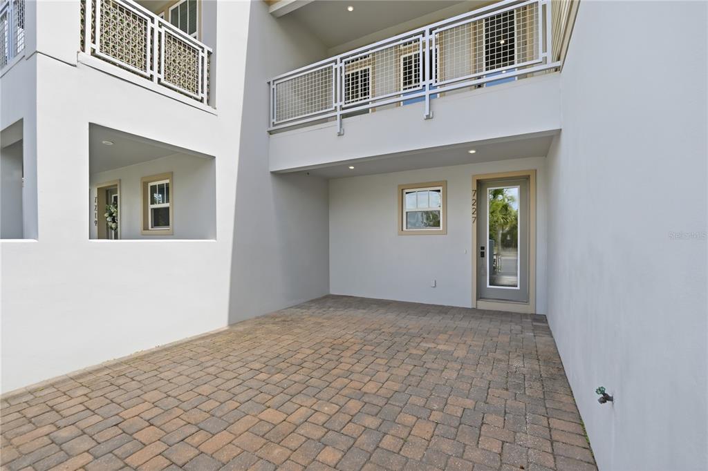 A paved courtyard sits between two white building sections with a glass-paneled door and balcony — 7227 NEMOURS PARKWAY, ORLANDO, FL