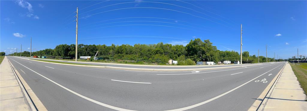 A panoramic view of a paved road intersection bordering a wooded lot with utility poles — 200 N HOAGLAND BOULEVARD, KISSIMMEE, FL