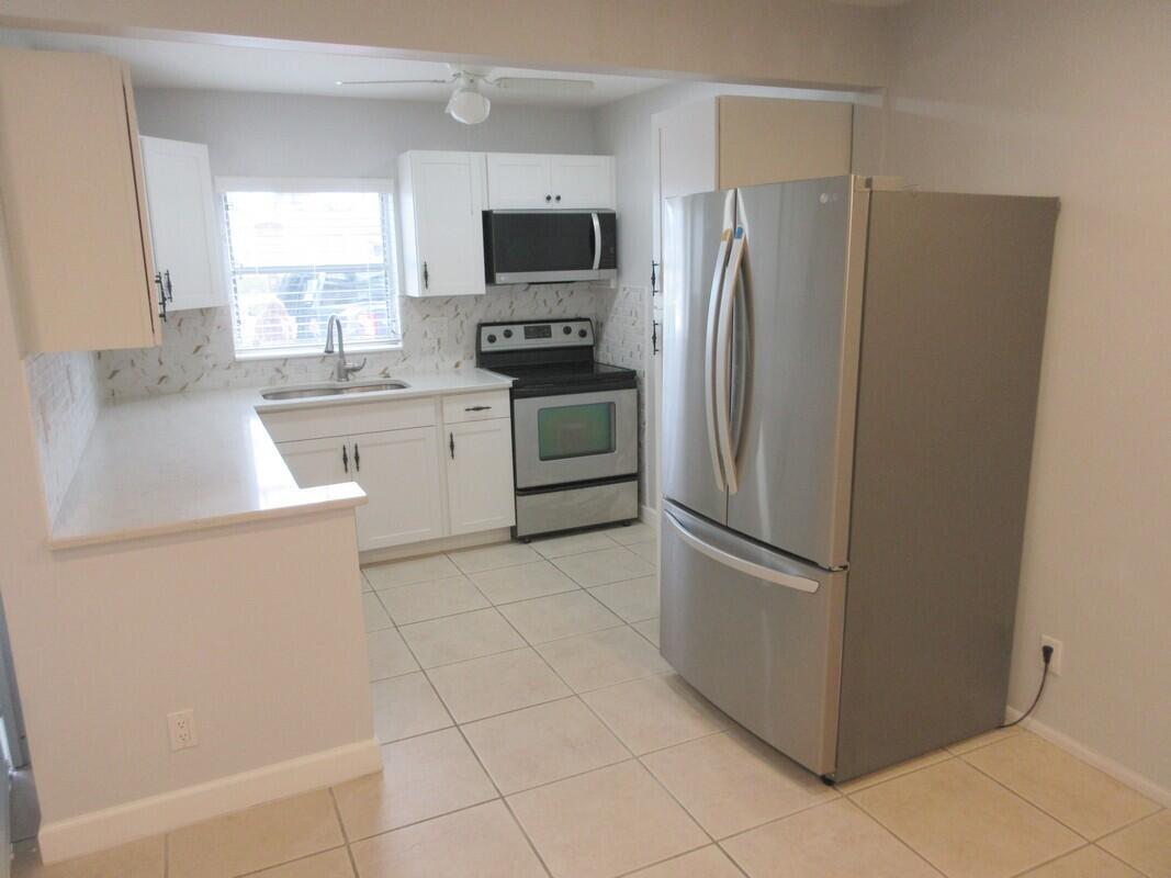 A kitchen with white cabinets, stainless steel appliances, light countertops, and beige tile flooring — 2572 Emory Drive E # J, West Palm Beach FL 33415, WEST PALM BEACH, FL