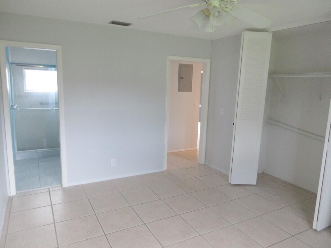 A bedroom with light gray walls, tile flooring, a ceiling fan, and an attached bathroom — 2572 Emory Drive E # J, West Palm Beach FL 33415, WEST PALM BEACH, FL