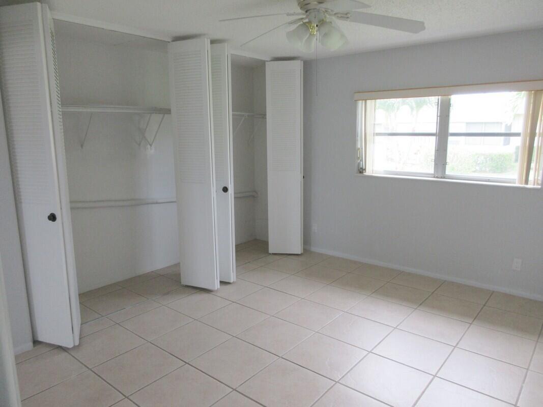 An empty bedroom with light-colored tile flooring, white walls, and two open louvered-door closets — 2572 Emory Drive E # J, West Palm Beach FL 33415, WEST PALM BEACH, FL