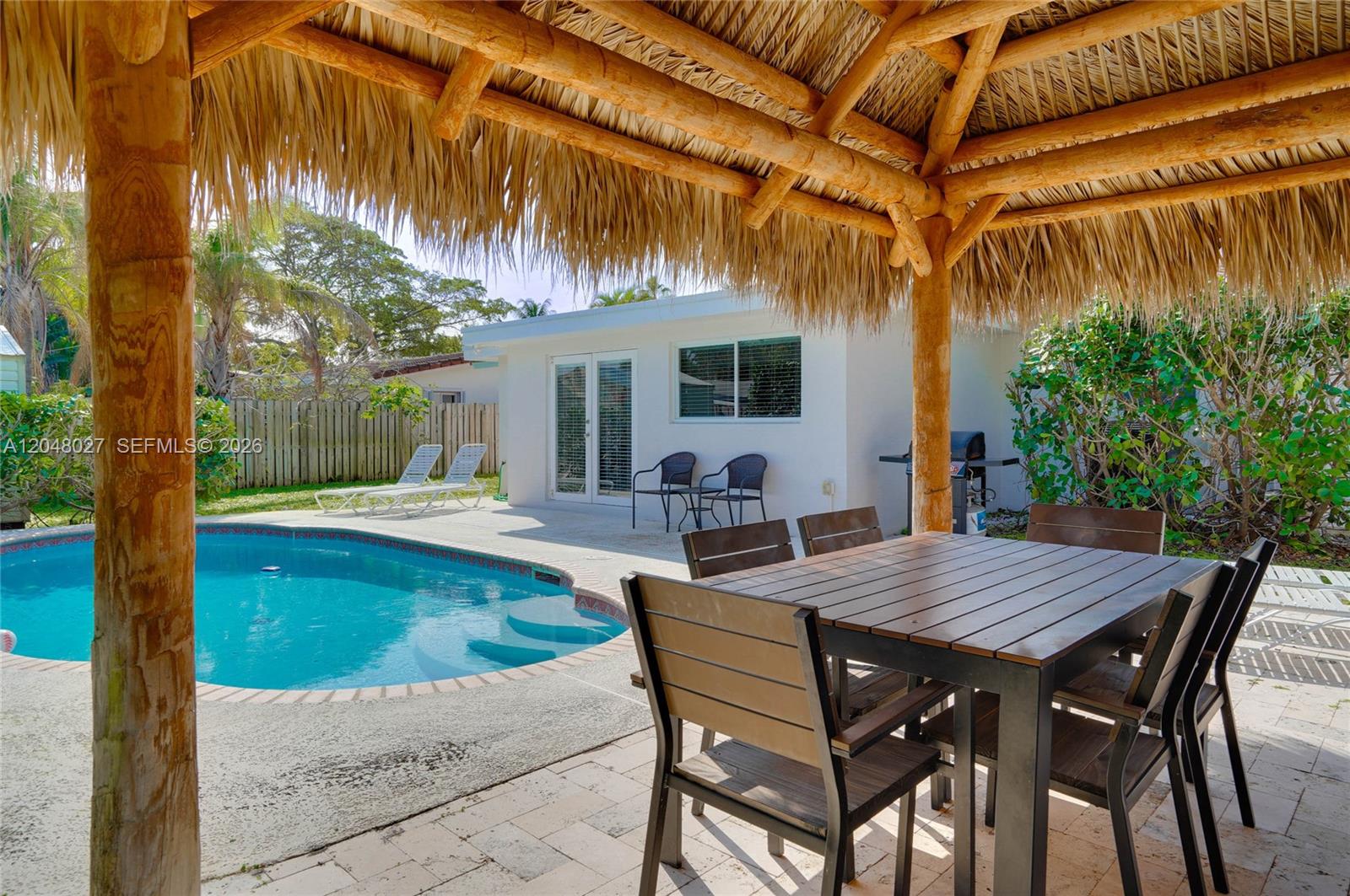 A backyard patio features a thatched-roof tiki hut, a swimming pool, and outdoor dining furniture — 1660 NE 26th Ave # 0, Pompano Beach FL 33062, POMPANO BEACH, FL