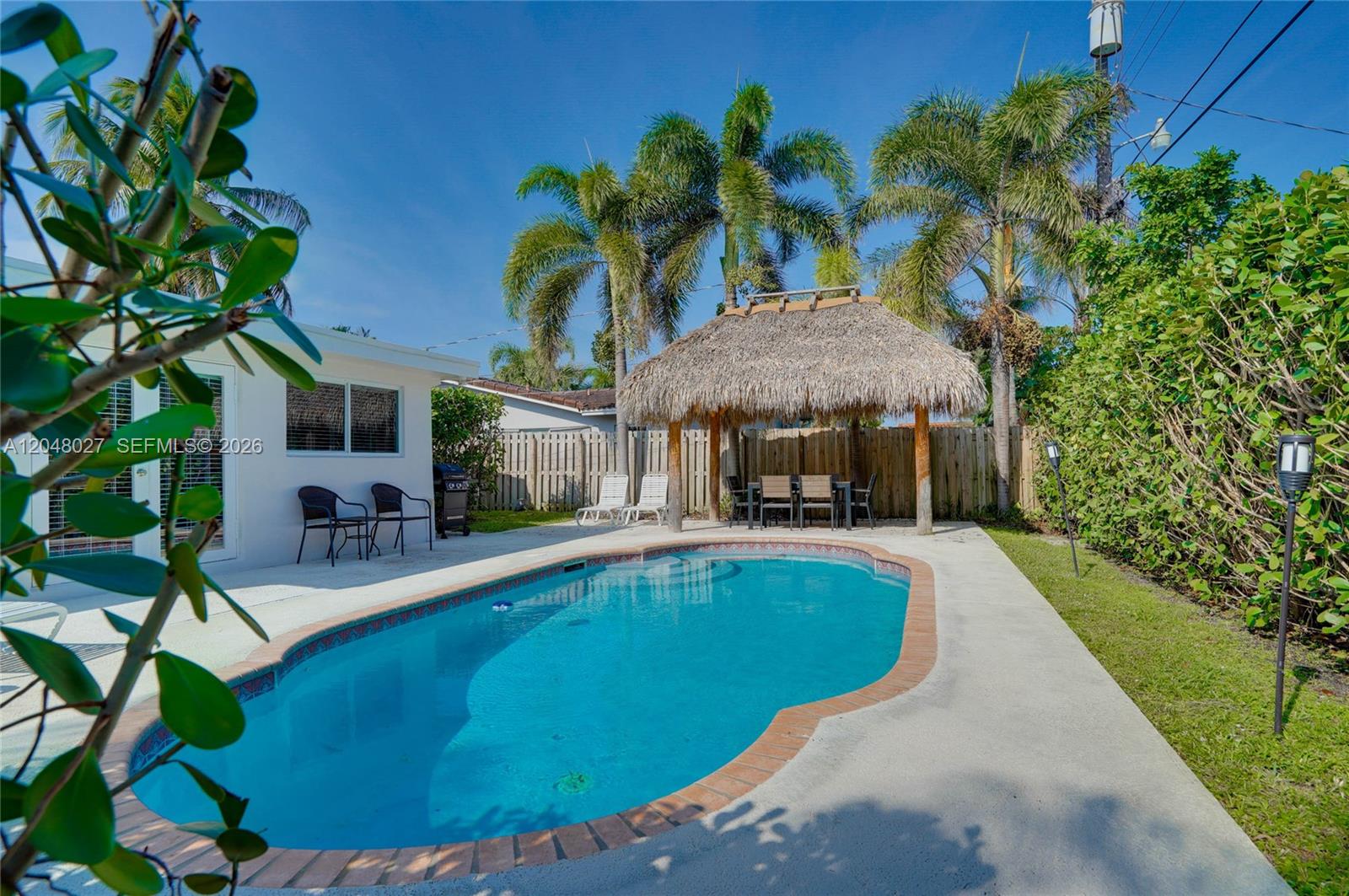 A backyard features a swimming pool, a thatched-roof tiki hut, and palm trees — 1660 NE 26th Ave # 0, Pompano Beach FL 33062, POMPANO BEACH, FL