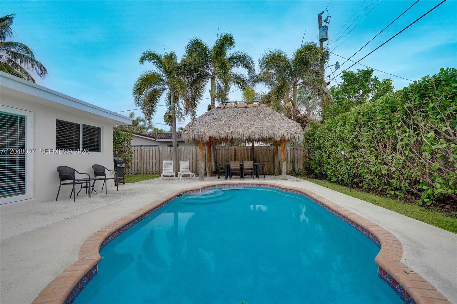 A backyard features a swimming pool, a thatched-roof tiki hut, and palm trees — 1660 NE 26th Ave # 0, Pompano Beach FL 33062, POMPANO BEACH, FL