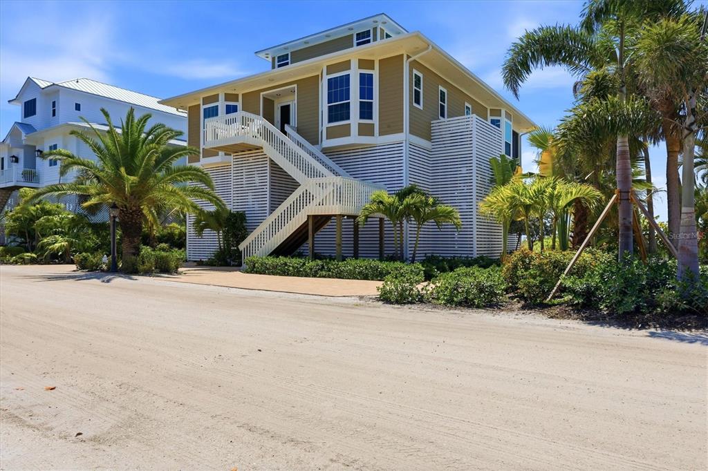 A tan elevated house with white stairs and lattice skirting sits beside a sandy road — 6950 PALM ISLAND DRIVE, PLACIDA, FL
