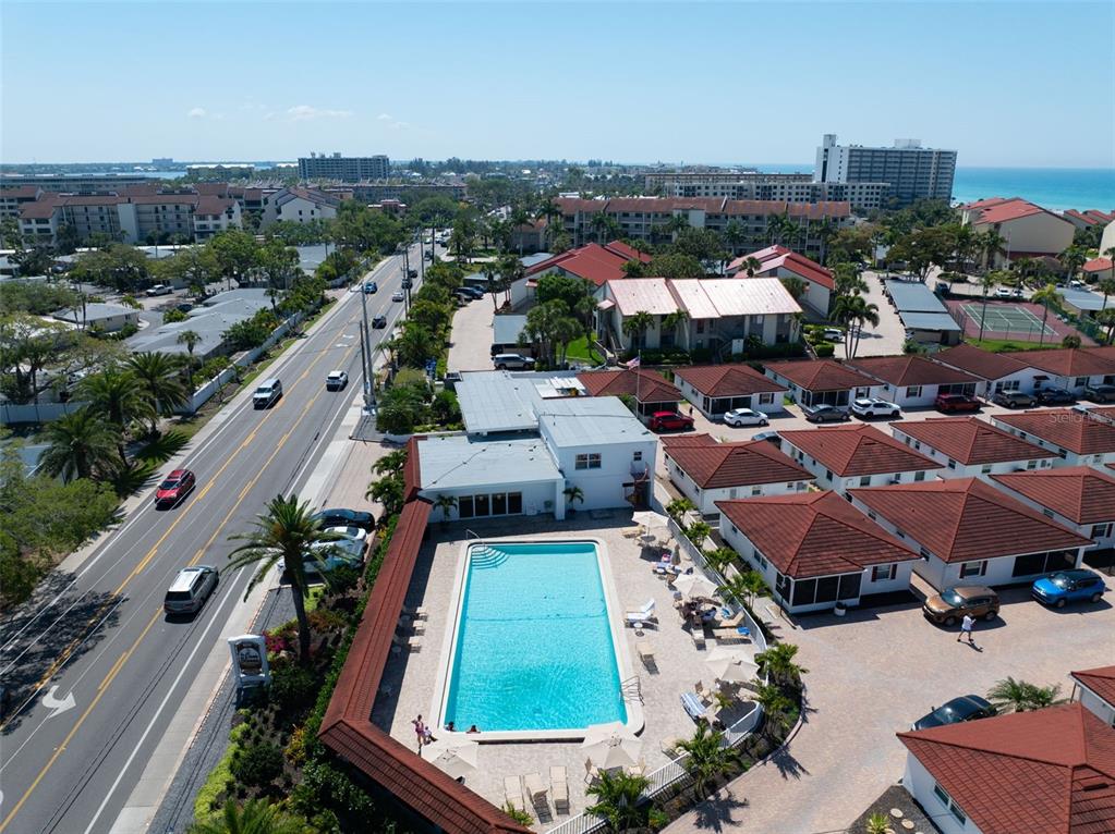 An aerial view shows a swimming pool surrounded by residential buildings and a nearby road — 6154 MIDNIGHT PASS ROAD UNIT A-05, SARASOTA, FL