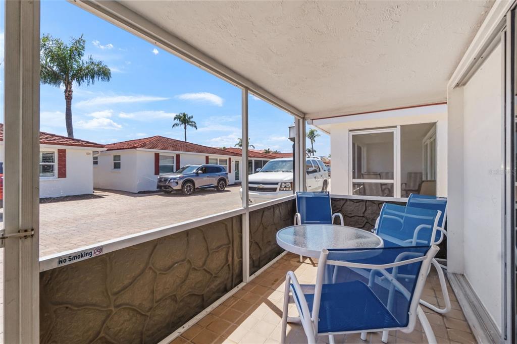 A screened-in patio features a small glass table, blue chairs, and a view of cars — 6154 MIDNIGHT PASS ROAD UNIT A-05, SARASOTA, FL