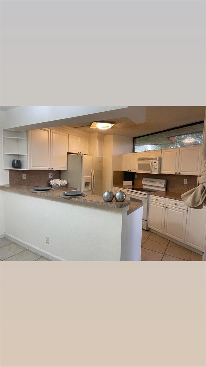 A kitchen features white cabinets, a breakfast bar, and tan countertops with tile flooring — 8159 Severn Drive # A, Boca Raton FL 33433, BOCA RATON, FL