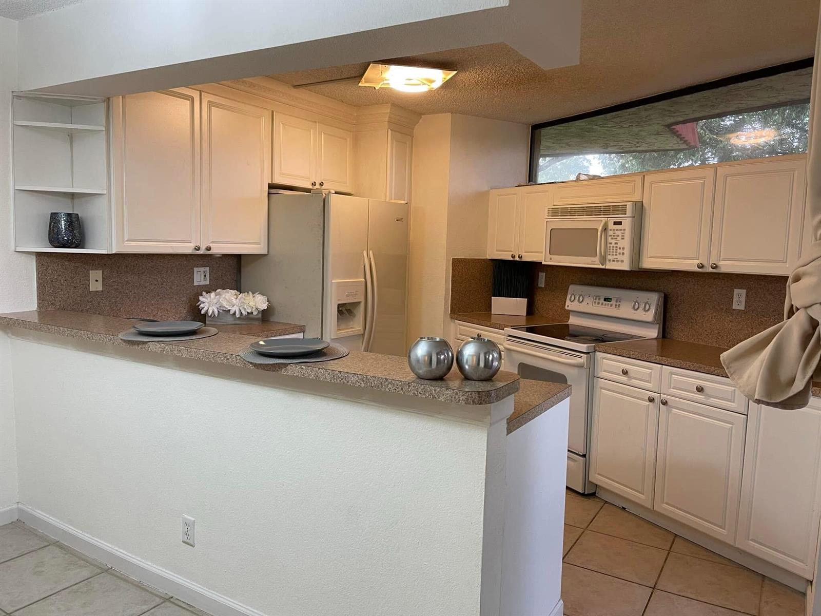 A kitchen features white cabinets, a speckled countertop, a breakfast bar, and stainless steel appliances — 8159 Severn Drive # A, Boca Raton FL 33433, BOCA RATON, FL
