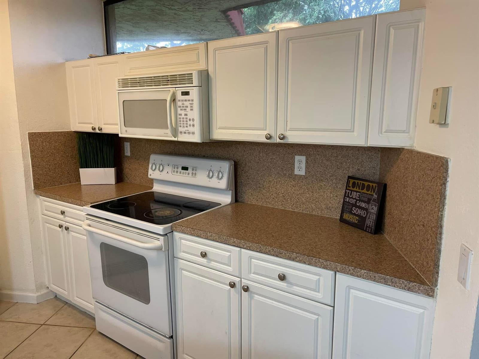 A kitchen features white cabinets, a white stove, a microwave, and brown speckled countertops — 8159 Severn Drive # A, Boca Raton FL 33433, BOCA RATON, FL