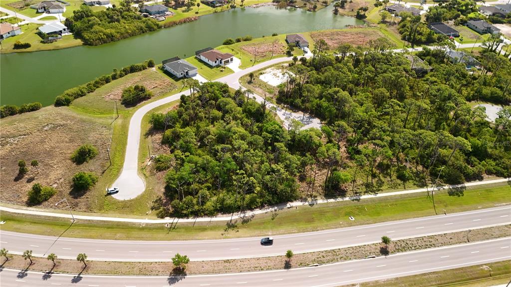An aerial view shows a wooded residential lot next to a road and a lake — 107 HAWK DRIVE, ROTONDA WEST, FL