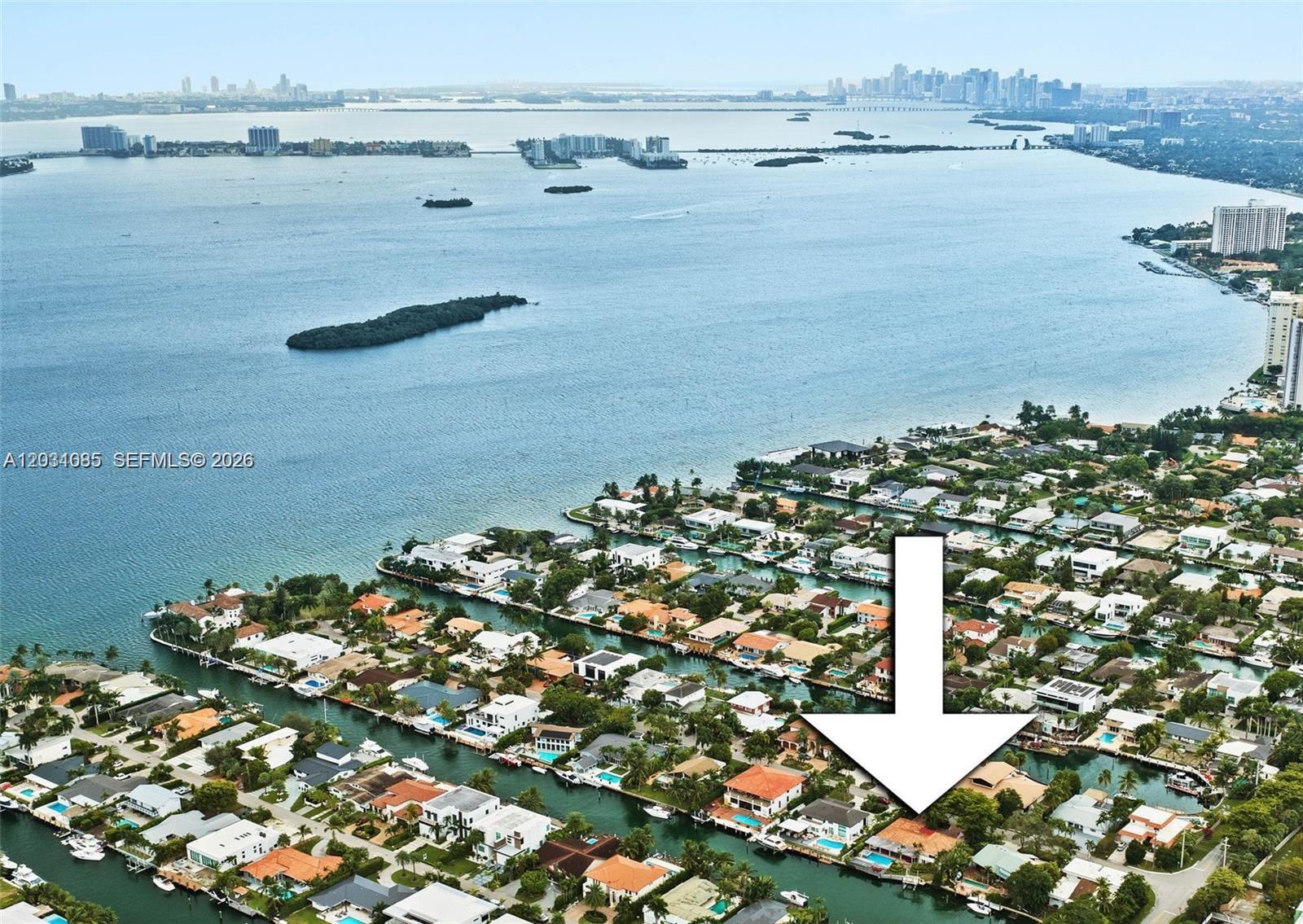 An aerial view shows a waterfront residential neighborhood with a large white arrow pointing downward — 2015 NE 120th Rd, North Miami FL 33181, NORTH MIAMI, FL