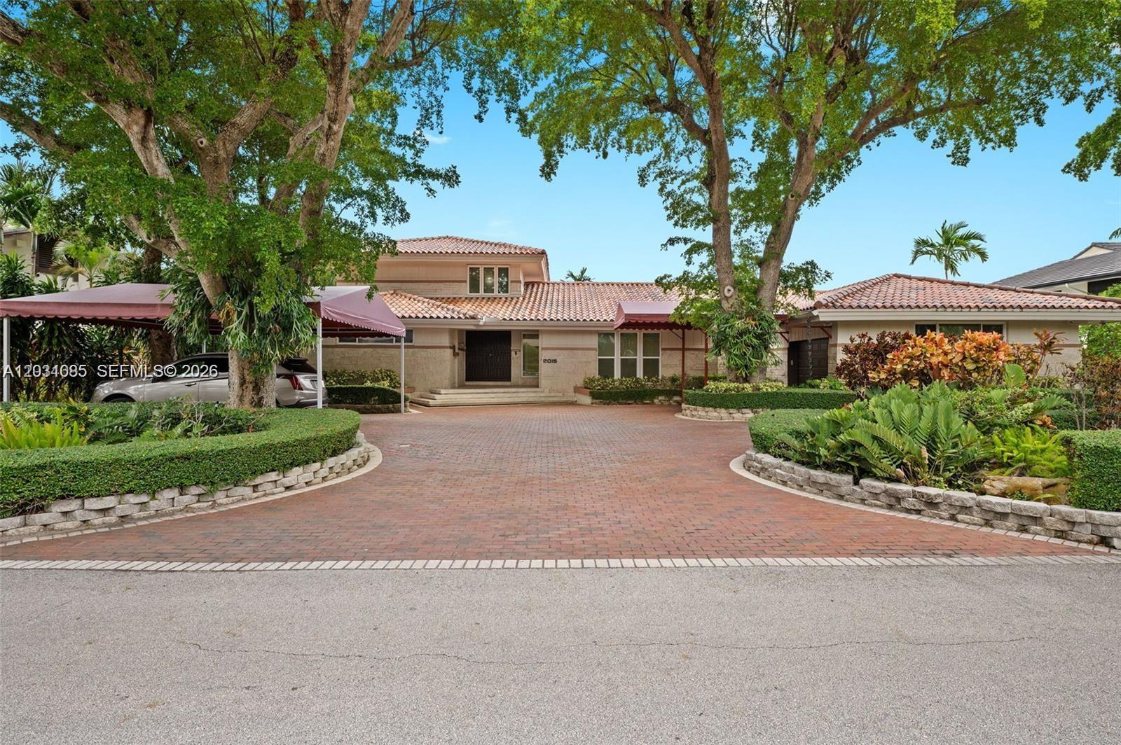 A large house with a brick driveway, red tile roof, and mature trees in front — 2015 NE 120th Rd, North Miami FL 33181, NORTH MIAMI, FL