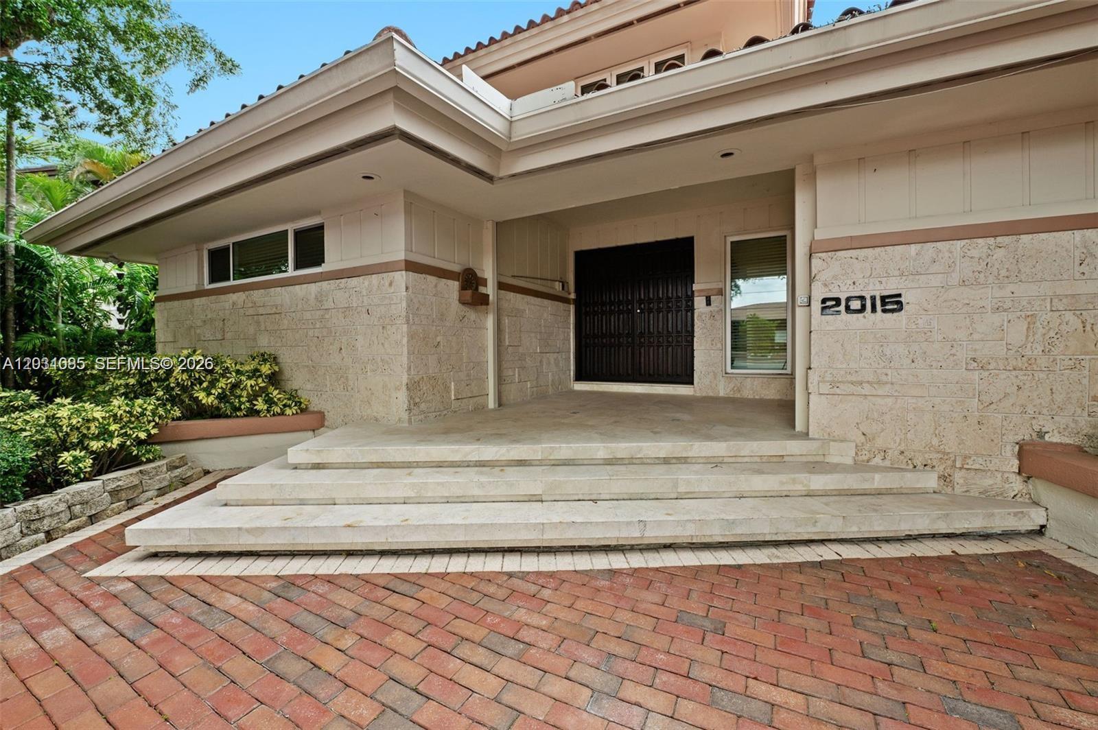 The exterior of a house features a stone facade, brick driveway, and double front doors — 2015 NE 120th Rd, North Miami FL 33181, NORTH MIAMI, FL