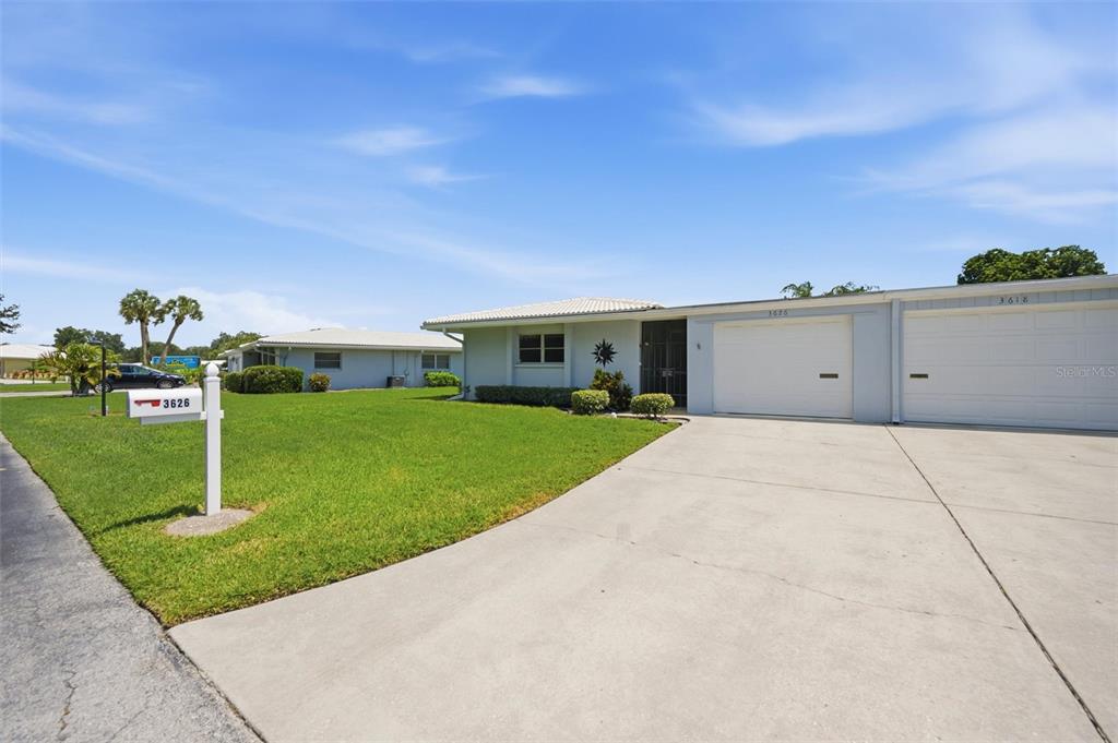A single-story duplex with a concrete driveway, white garage doors, and a green lawn — 3626 MEDFORD LANE UNIT 1537, SARASOTA, FL