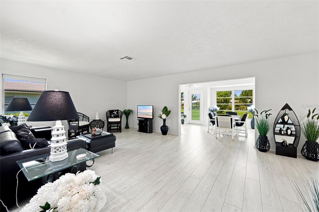 A bright living room features white walls, light wood-look flooring, and an adjacent dining area — 3626 MEDFORD LANE UNIT 1537, SARASOTA, FL