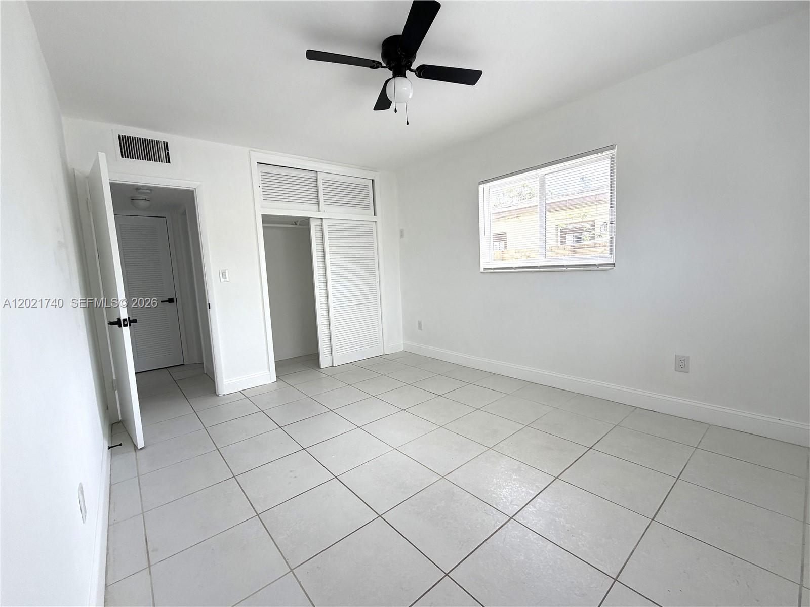 A bedroom with white walls, light tile flooring, a ceiling fan, and a closet — NORTH MIAMI BEACH, FL