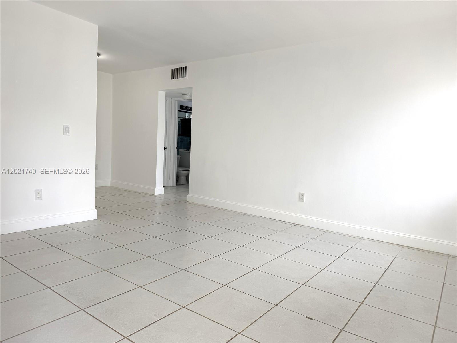 An empty room features white walls, light-colored tile flooring, and a doorway leading to a bathroom — NORTH MIAMI BEACH, FL