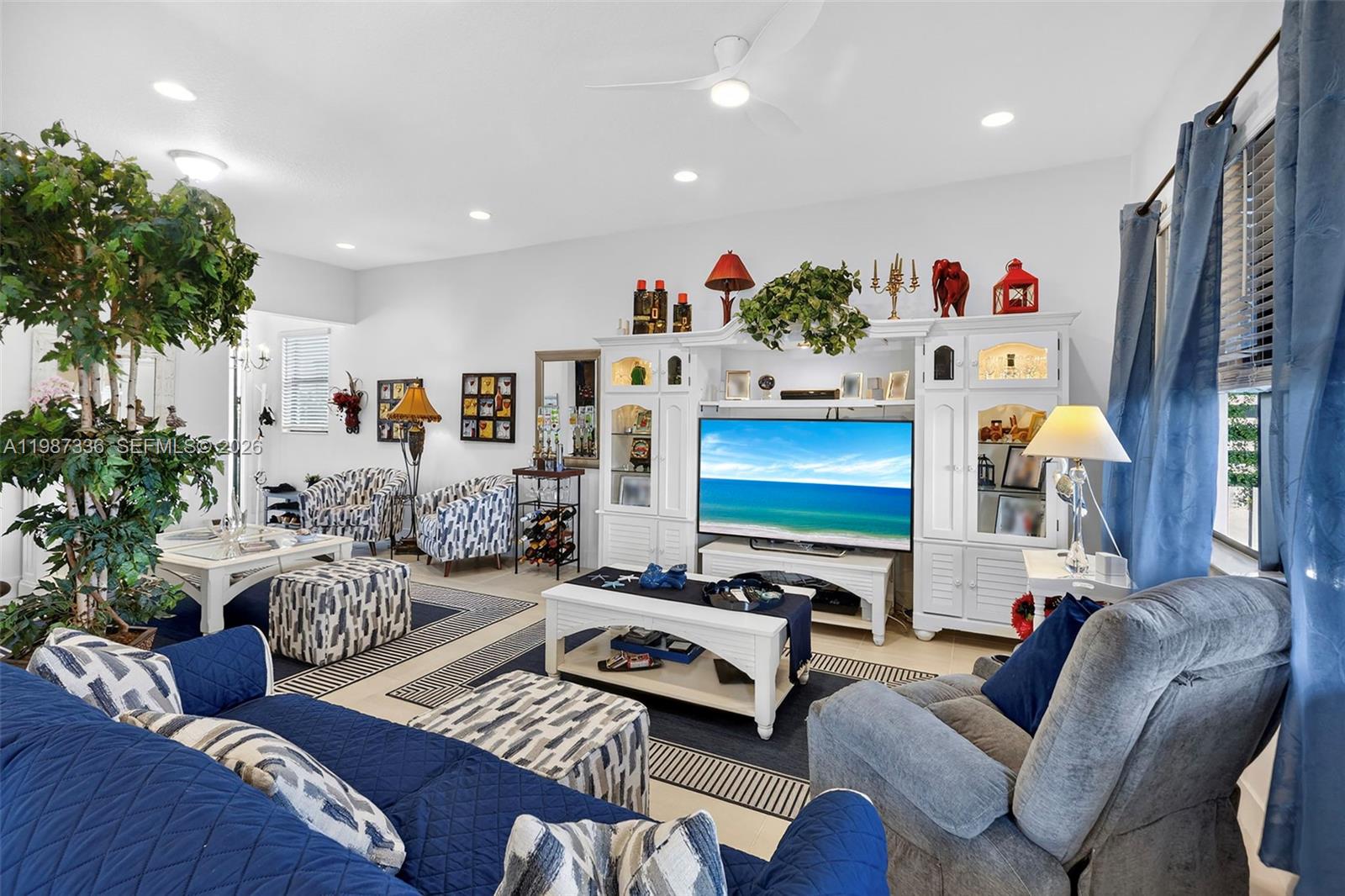 A living room features a white entertainment center, blue furniture, and a large indoor tree — 5700 Argento, Ave Maria FL 34142, AVE MARIA, FL