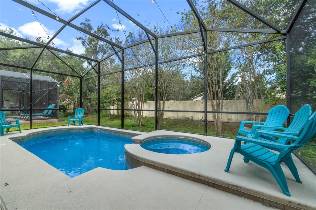 A screened-in pool and spa area with blue chairs on a concrete patio — 2652 SANTOSH COVE, KISSIMMEE, FL