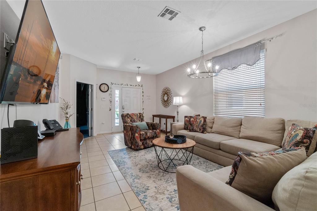 A living room features a beige sectional sofa, patterned armchair, area rug, and chandelier — 2652 SANTOSH COVE, KISSIMMEE, FL