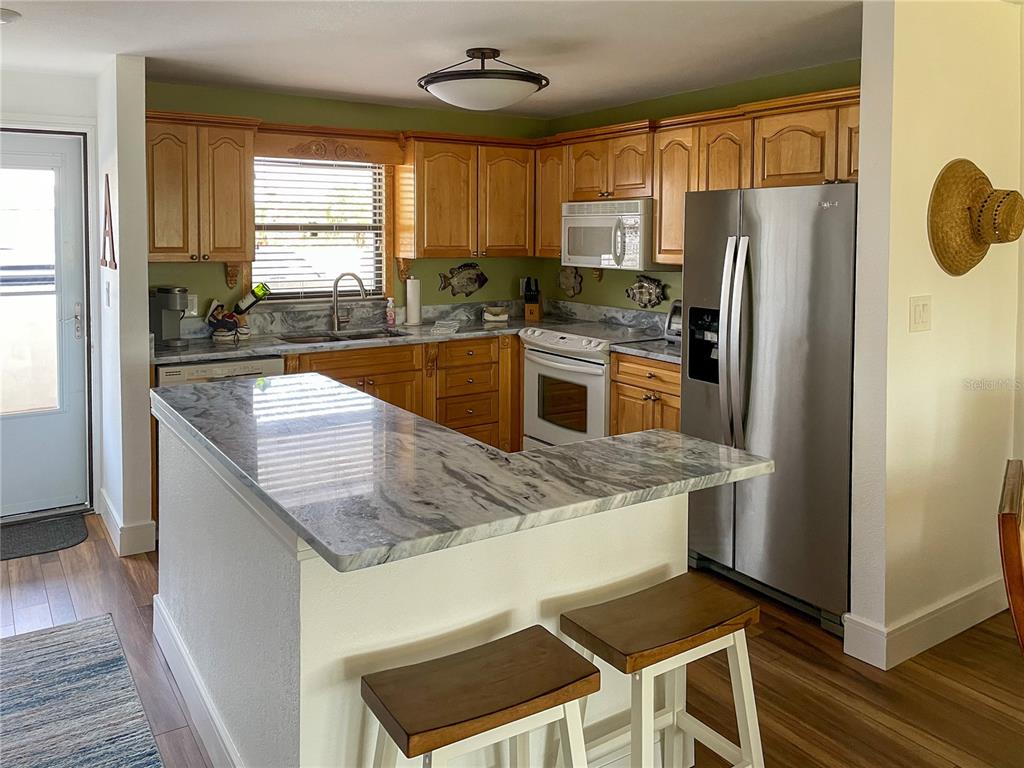 A kitchen features wood cabinets, marble-patterned countertops, stainless steel appliances, and a breakfast bar — 1230 GULF BOULEVARD UNIT 207, CLEARWATER BEACH, FL