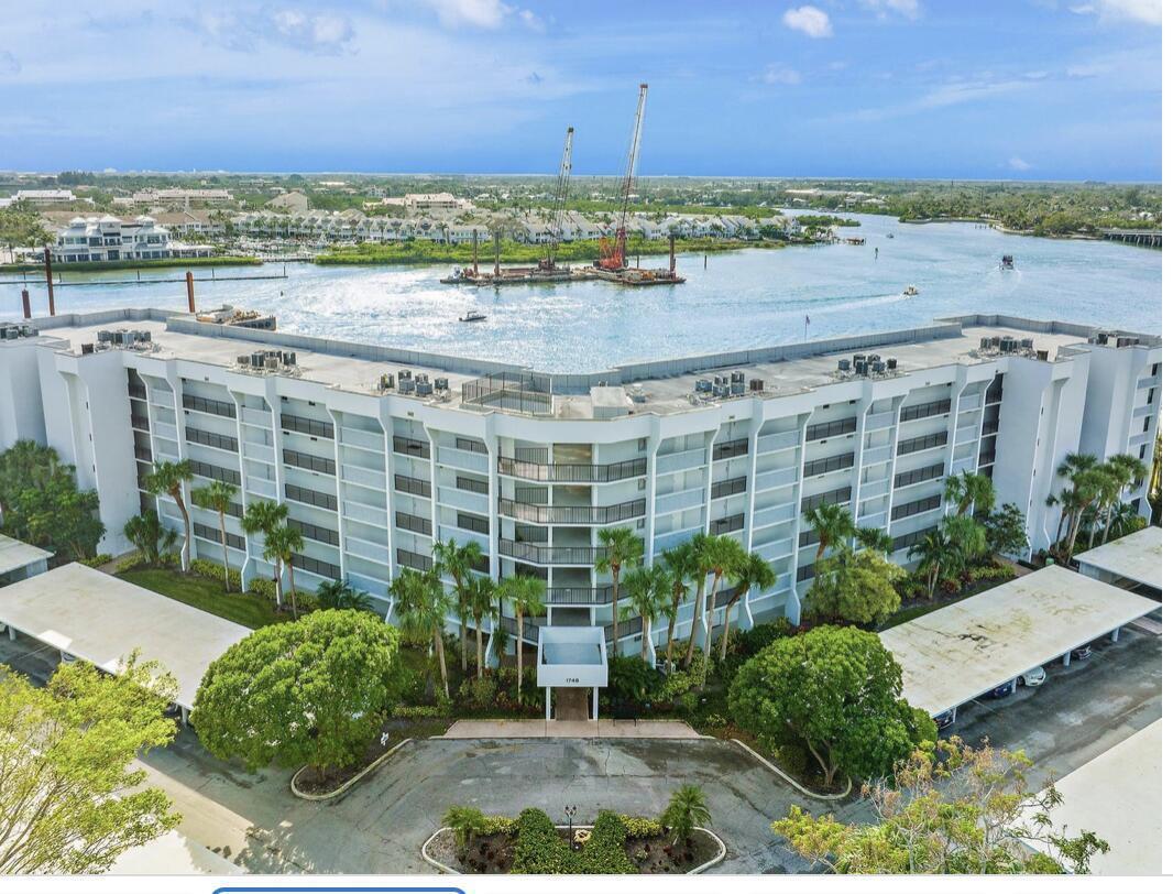 An aerial view of a multi-story white apartment building situated along a waterfront with construction equipment — 1748 Jupiter Cove Drive # A, Jupiter FL 33469, JUPITER, FL