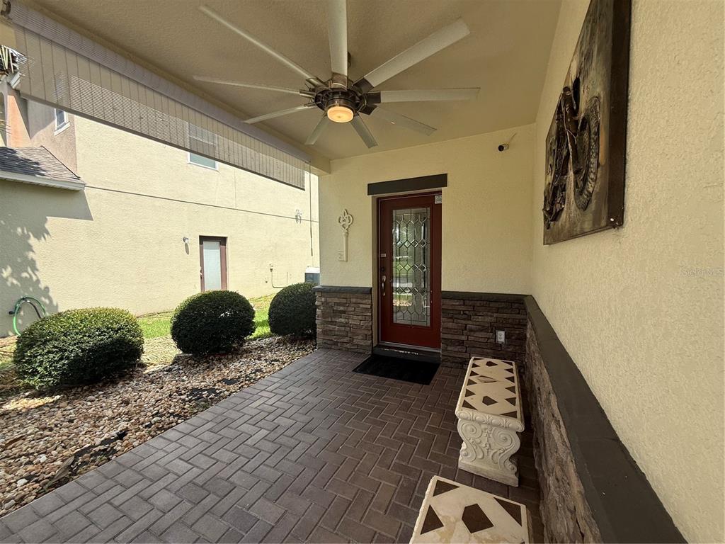 A covered front porch features a red door, stone accents, a ceiling fan, and pavers — 2706 MONTICELLO WAY, KISSIMMEE, FL